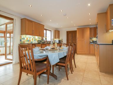 A kitchen with wooden cabinets and dining table set for four near doors at Meadowside in Goonhavern