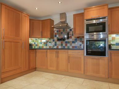 A kitchen with wooden cabinets and drawers a stainless steel oven and microwave and a tiled backsplash at Meadowside in Goonhavern