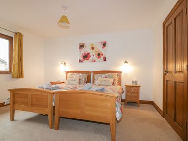 A bedroom with two single beds with wooden frames bedside tables and a floral painting on the wall at Meadowside in Goonhavern