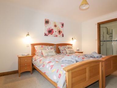 A bedroom with a wooden double bed two bedside tables with lamps and an open door to a bathroom at Meadowside in Goonhavern