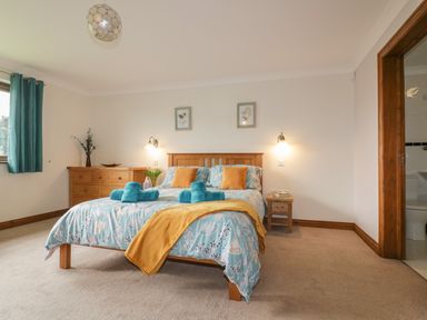A bedroom with a bed with blue and yellow bedding beside a wooden dresser and nightstand at Meadowside in Goonhavern