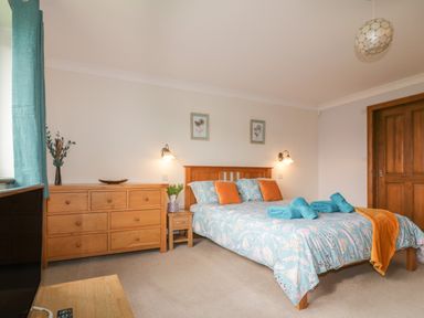 A bedroom with a bed with patterned bedding and orange pillows next to a wooden chest of drawers at Meadowside in Goonhavern