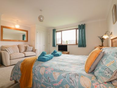 A bedroom with a double bed sofa and a window with curtains at Meadowside in Goonhavern