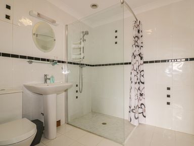 A bathroom with a toilet sink shower area with glass panel and floral shower curtain at Meadowside in Goonhavern
