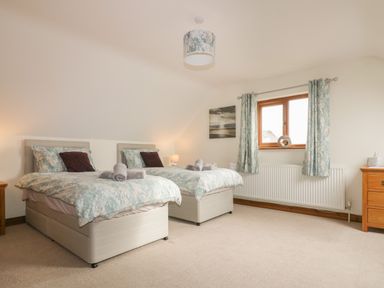 A bedroom with two single beds side by side two bedside tables a window with curtains and a ceiling light at Meadowside in Goonhavern