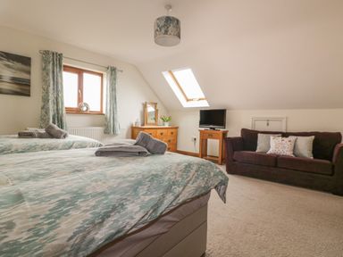 A bedroom with two beds a wooden dresser with a mirror a flat screen television on a wooden stand and a sofa at Meadowside in Goonhavern