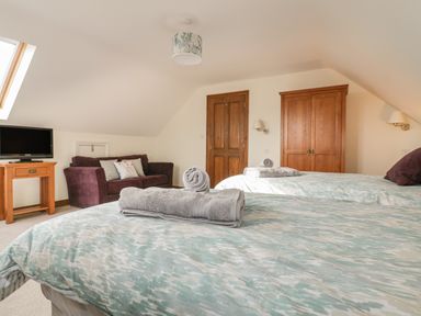 A bedroom with two beds with towels on them a wooden wardrobe a wooden door a purple sofa a wooden table with a television and a skylight window at Meadowside in Goonhavern