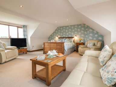 A bedroom with a wooden bed and bedside table and two armchairs and a sofa and a wooden coffee table with tea set and croissants at Meadowside in Goonhavern