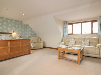 A bedroom with a wooden bed armchair beige sofa and wooden coffee table at Meadowside in Goonhavern