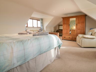 A bedroom with a bed sofa wooden wardrobe and armchair at Meadowside in Goonhavern