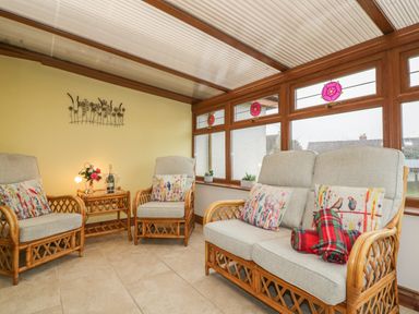 A seating area with two armchairs sofa cushions and a side table with flowers and drinks at Meadowside in Goonhavern