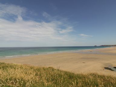 A grassy hill overlooking a sandy beach and ocean under a partly cloudy sky at Meadowside in Goonhavern