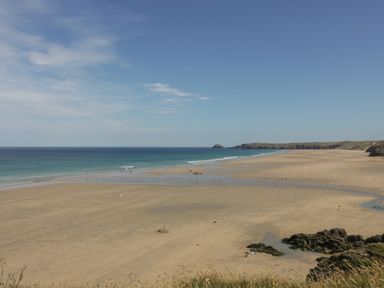 A sandy beach with people near the shoreline and rocky areas at Meadowside in Goonhavern