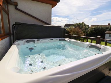 An outdoor hot tub with water bubbling next to a house with a wooden railing and trees in the background at Meadowside in Goonhavern