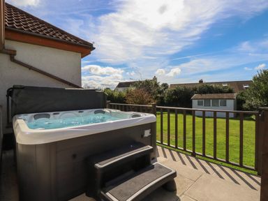 An outdoor patio with a hot tub and steps overlooking a grassy yard and a small white shed at Meadowside in Goonhavern