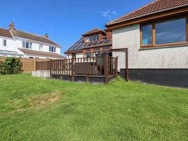 A backyard with a wooden deck attached to a house with solar panels on the roof at Meadowside in Goonhavern