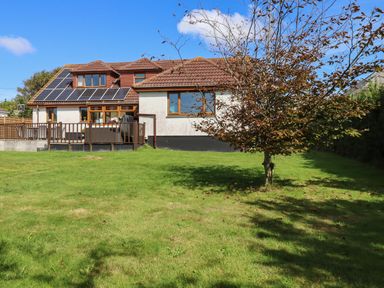 A house with solar panels on the roof and a deck in a garden with a tree at Meadowside in Goonhavern