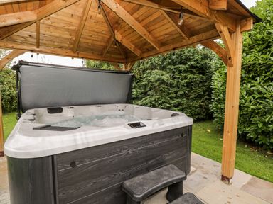 An outdoor hot tub with bubbling water under a wooden pavilion surrounded by greenery at Reybridge House in Lacock