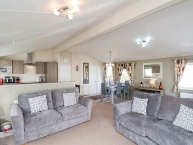 An open living area with two grey sofas a dining table and chairs a kitchen with cabinets and appliances at Two Little Ducks in Cayton