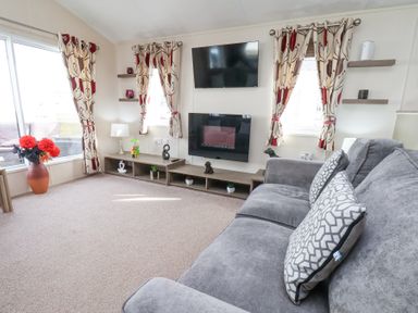 A living room with a grey sofa patterned curtains and a wall-mounted television at Two Little Ducks in Cayton