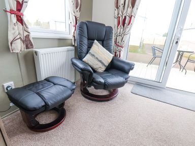 A black leather armchair with a cushion and matching footstool near a window and glass door at Two Little Ducks in Cayton