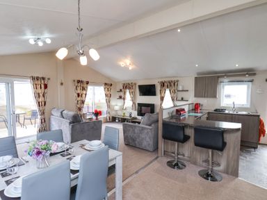 An open-plan living room and kitchen area with sofas, dining table, bar stools, and kitchen cabinets at Two Little Ducks in Cayton