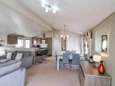 An open living room and kitchen with gray sofas dining table and chairs and wooden cabinets at Two Little Ducks in Cayton