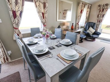 A dining area with a table set for six and a lounge chair with footstool at Two Little Ducks in Cayton