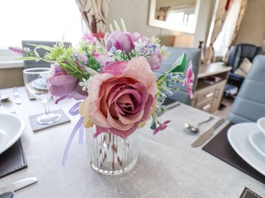 A dining table with a flower arrangement in a glass vase plates glasses cutlery and chairs at Two Little Ducks in Cayton