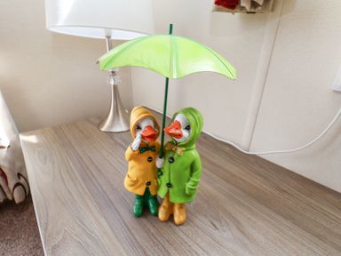 A wooden table with two duck figurines wearing raincoats and holding an umbrella at Two Little Ducks in Cayton