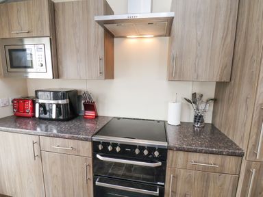 A kitchen with wooden cabinets stove microwave red toaster black air fryer knife set paper towel and cooking utensils at Two Little Ducks in Cayton