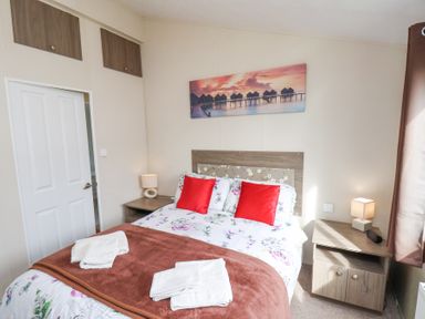 A bedroom with a double bed with floral bedding and red pillows two bedside tables with lamps a door and a wall painting at Two Little Ducks in Cayton