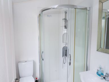 A bathroom with a corner shower enclosure a toilet and a sink with a mirror and soap dispenser at Two Little Ducks in Cayton
