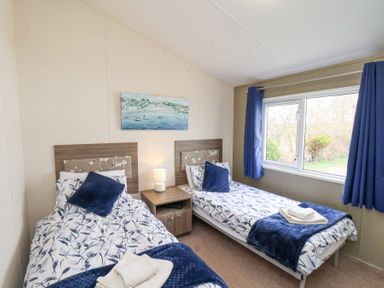 A bedroom with two single beds blue pillows and curtains and a painting above a nightstand at Two Little Ducks in Cayton