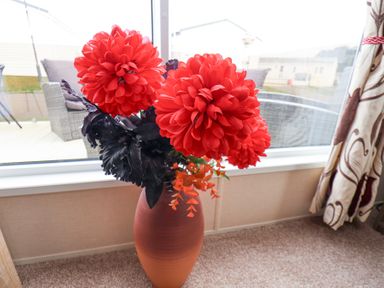 A vase with large red flowers on the floor in front of a window with curtains at Two Little Ducks in Cayton