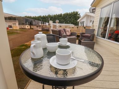 An outdoor seating area with a glass table set with white cups a teapot and a bowl and wicker chairs at Two Little Ducks in Cayton