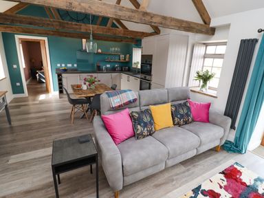 An open living room and kitchen with a gray sofa and colorful cushions at The Roost in Porthallow