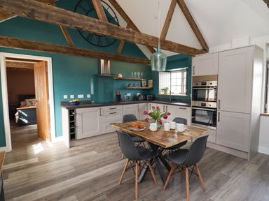 A kitchen with a wooden dining table set with flowers and cups and grey chairs at The Roost in Porthallow