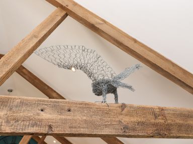 A wire sculpture of a bird on a wooden beam in a room with white ceiling at The Roost in Porthallow