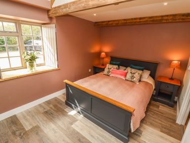 A bedroom with a double bed flanked by two bedside tables with lamps and a window with flowers on the sill at The Roost in Porthallow