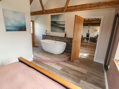 A bedroom with a bed and a bathtub on a raised platform with paintings on the wall at The Roost in Porthallow