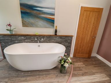 A bathroom with a freestanding bathtub flowers on the floor and a wooden door at The Roost in Porthallow