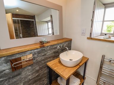 A bathroom with a round sink on a wooden countertop a large mirror and a window at The Roost in Porthallow