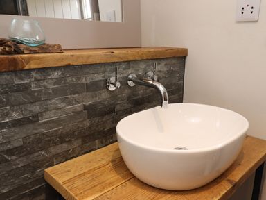A bathroom sink with wall-mounted faucet and wooden countertop at The Roost in Porthallow