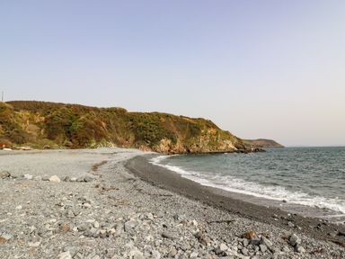 A rocky beach with waves and green cliffs at The Roost in Porthallow