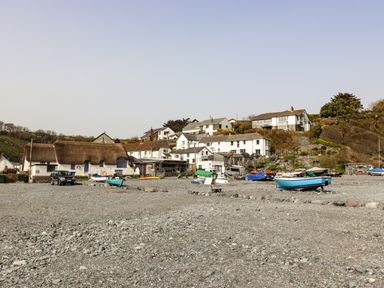 A beach with boats on pebbles and houses on a hillside at The Roost in Porthallow