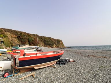 A pebble beach with several boats and a rocky cliff by the sea at The Roost in Porthallow