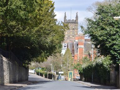 A street with trees on both sides and a large historic building in the background at The Escape in Malvern