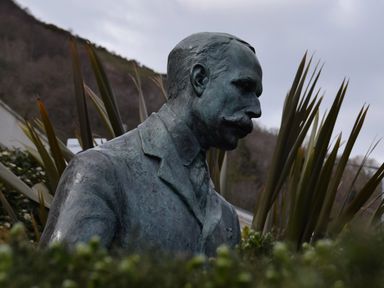 A bronze bust statue of a man with a mustache surrounded by tall plants outdoors at The Escape in Malvern