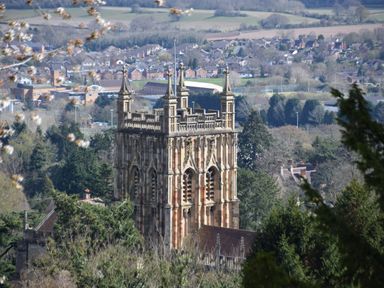 A gothic church tower surrounded by trees with a town and fields in the background at The Escape in Malvern